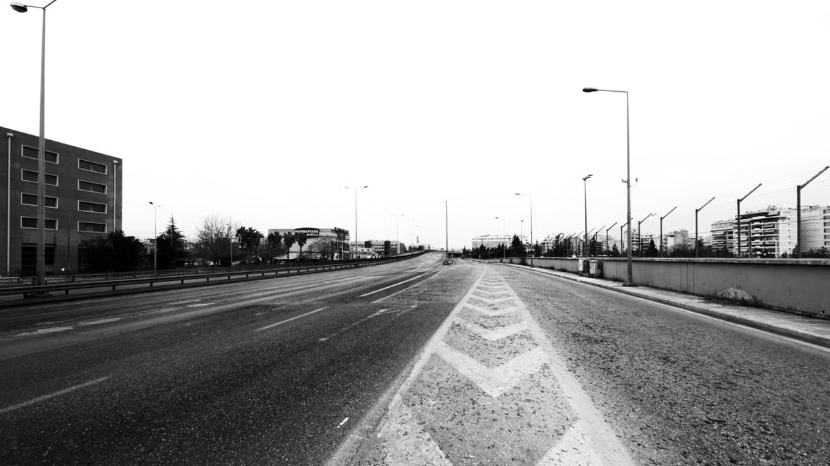 Monochrome photo of an empty urban road with buildings and street lamps, showcasing cityscape.